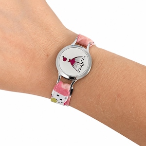 May include: A circular silver-toned metal charm bracelet featuring a central disc with a magenta graphic of a stylised flower or jellyfish. The bracelet band is made of fabric with a pattern of pink, white, black dots, and green accents.