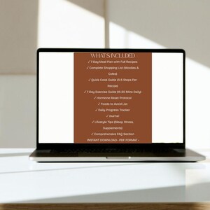 May include: A laptop displays a brown graphic with white text listing the contents of a digital download. The text includes a 7-day meal plan, shopping list, exercise guide, and more. The laptop is on a white surface.