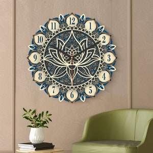 Puede incluir: Un reloj de pared de madera con un diseño de mandala azul y blanco que presenta una flor de loto en el centro. El reloj tiene números romanos y manecillas negras.