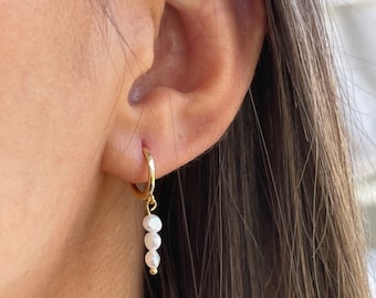 Pode incluir: Brincos de argola dourados com um charme pendente de três pérolas brancas.