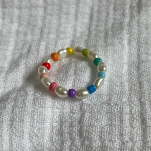 May include: A rainbow beaded bracelet with white pearl beads. The bracelet is made with small, colorful beads in a rainbow pattern.