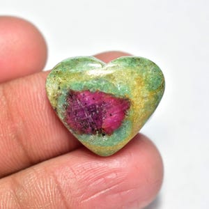Peut inclure: Une pierre précieuse en forme de cœur avec un centre rose vif entouré d'un extérieur vert et jaune. La pierre polie est tenue dans une main, mettant en valeur ses couleurs naturelles et son motif unique. La pierre précieuse est un bijou unique.