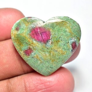Peut inclure: Une pierre précieuse en forme de cœur, avec une base verte et des inclusions rouges vives. La surface polie révèle les motifs naturels. La pierre est tenue dans une main. Idéale pour la bijouterie ou la décoration.