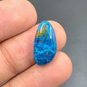 Könnte beinhalten: Ein tropfenförmiger Cabochon-Edelstein mit einem blauen und grünen Farbmuster. Der Stein hat eine glatte, polierte Oberfläche und ist in einen silbernen Ring gefasst.