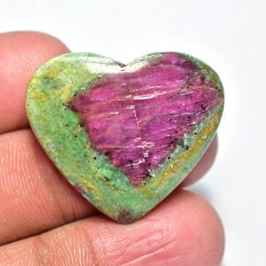 May include: Heart-shaped gemstone with a vibrant color palette. The stone features a striking combination of green and magenta hues. The heart-shaped stone is held in a hand, showcasing its natural beauty and unique color variations.