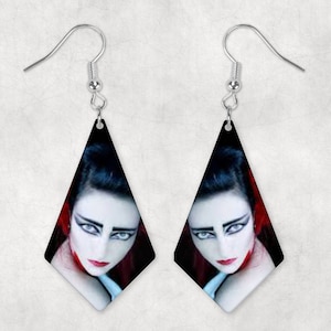 May include: A pair of silver dangle earrings with a diamond-shaped design. Each earring features a black and white image of a woman with dark hair and dramatic makeup.
