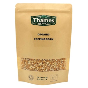 May include: A brown paper bag with a clear window showing organic popping corn. The bag has a green and white label that says "Thames Organic" and "Organic Popping Corn". The bag also has a green and white label that says "Premium Quality" and a green and white seal that says "Soil Association Organic".