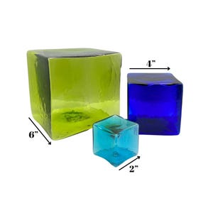May include: Three glass cubes in shades of green, blue, and teal. The largest cube is 6 inches, the medium cube is 4 inches, and the smallest cube is 2 inches. The cubes have a textured appearance and are arranged on a white background.