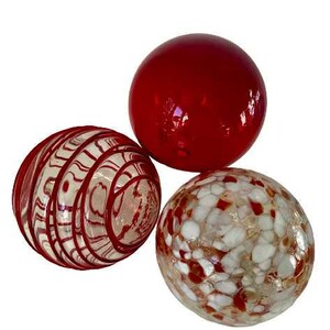 May include: Three decorative glass spheres. One is solid red, another is clear with red swirls, and the third is white with red and brown speckles. The spheres are arranged on a white background.