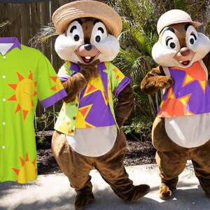 Pode incluir: Dois personagens Chipmunk vestindo camisas havaianas coloridas com sóis amarelos e detalhes roxos. As camisas têm frente abotoada e mangas curtas. Um Chipmunk está usando um chapéu de palha e o outro está usando um boné de beisebol branco.