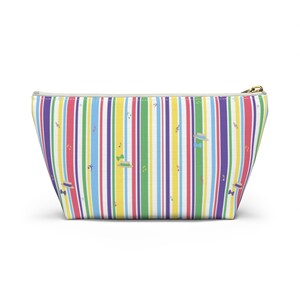 May include: A colorful cosmetic bag with vertical stripes in red, purple, blue, green, yellow, and white. The bag features a gold zipper and a pattern of hats, musical notes, and bow ties.