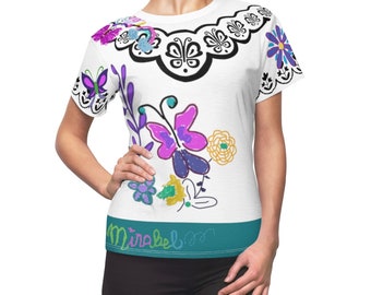 Könnte beinhalten: Weißes T-Shirt mit einem farbenfrohen Blumen- und Schmetterlingsdesign. Das Shirt hat einen türkisfarbenen Band am unteren Rand mit dem Text "Mirabel" in einer bunten Schrift.