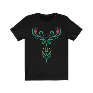 Könnte beinhalten: Schwarzes T-Shirt mit einem grünen, violetten und rosafarbenen Blumendesign. Das Design zeigt stilisierte Blumen und Blätter.