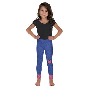 Puede incluir: Una niña pequeña con una camiseta negra de manga corta y leggings de mezclilla azul con un diseño de gato rosa en la rodilla. Los leggings tienen puños rosas.
