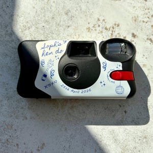 Personalised hen party disposable camera wrap with blue line art illustrations on a Kodak FunSaver camera.  Shown on a brown stone background with the light catching the details in an editorial fashion.