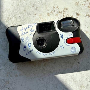 Personalised hen party disposable camera with wrap finished with blue line art illustrations on a Kodak FunSaver camera.  Shown on a brown stone background with the light catching the details in an editorial fashion.