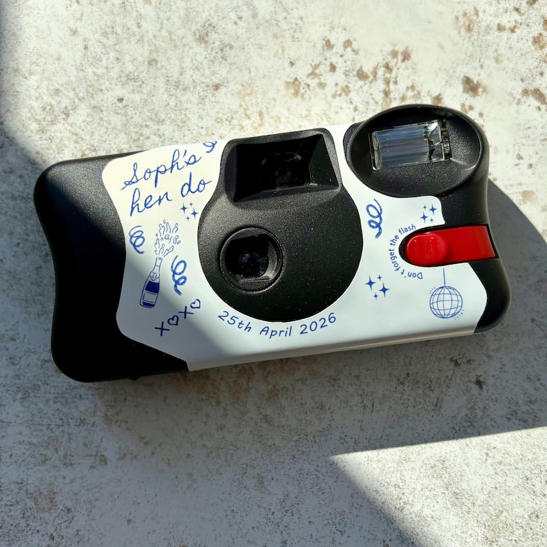 Personalised hen party disposable camera with wrap finished with blue line art illustrations on a Kodak FunSaver camera.  Shown on a brown stone background with the light catching the details in an editorial fashion.
