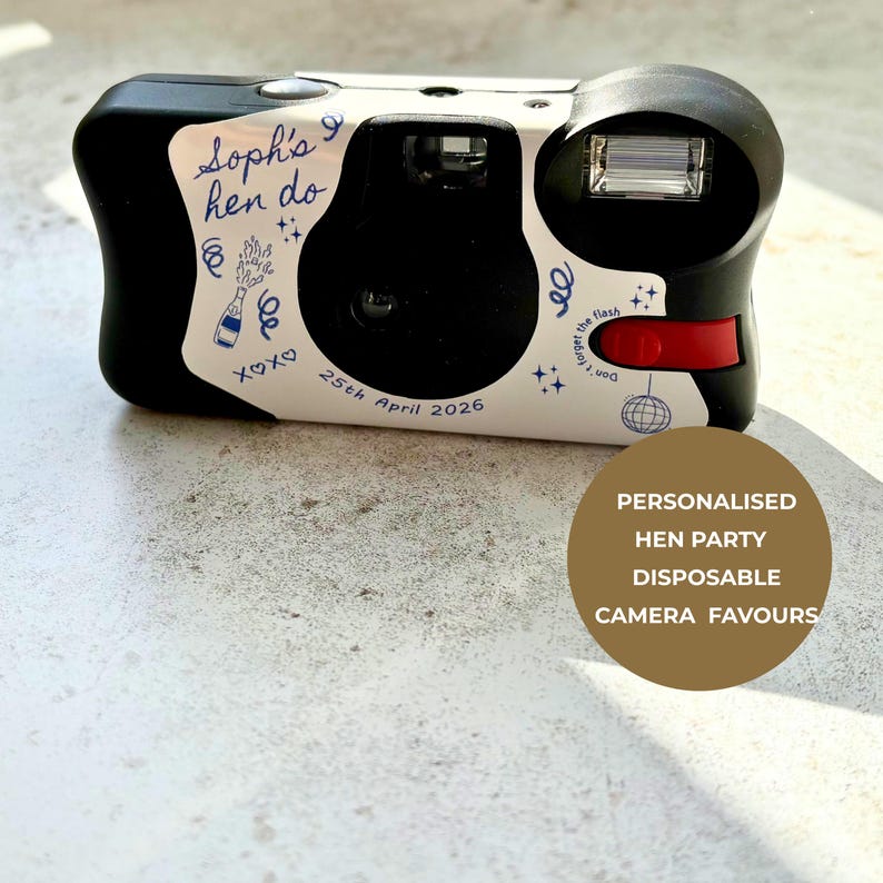 May include: A black disposable camera with a white custom wrap featuring blue line art of a champagne bottle, a disco ball, and stars. The text reads "Soph's hen do", "25th April 2026", and "Don't forget the flash". It includes a red shutter button.