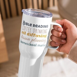 May include: White stainless steel travel mug with a black handle. The mug has the text "Bible Reading, Coffee Drinking, Oil Diffusing, Lesson Planning, Homeschool Mama" printed on it in gold and blue.