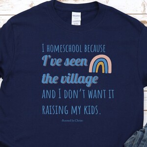 May include: Navy blue t-shirt with a rainbow graphic and the text "I homeschool because I've seen the village and I don't want it raising my kids. -Rooted In Christ- "