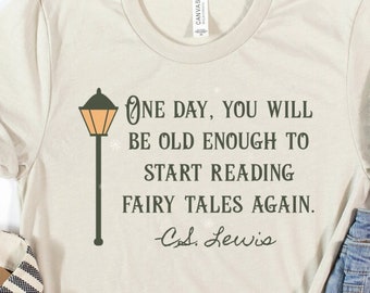May include: A cream-colored t-shirt with the quote "One day, you will be old enough to start reading fairy tales again." and a street lamp graphic. The shirt is paired with denim shorts, a beige hat, and striped sandals.