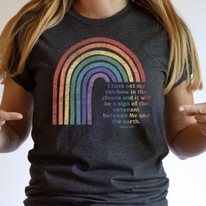 Pu&ograve; includere: Una maglietta grigio scuro con una grafica arcobaleno e il testo "Ho posto il mio arcobaleno nelle nuvole, e sar&agrave; segno dell'alleanza tra me e la terra. Genesi 9:13"