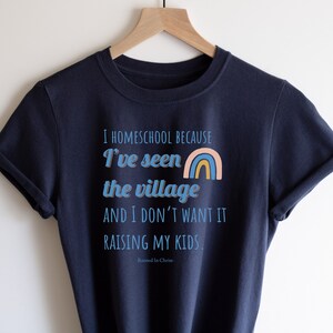 May include: A navy blue t-shirt with the text "I homeschool because I've seen the village and I don't want it raising my kids." and a rainbow graphic. The text "Rooted in Christ" is also included.