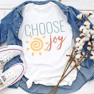 May include: White t-shirt with the text "CHOOSE joy" in blue, orange, and yellow. A stylised sun with a yellow centre and orange rays is to the left of the text.