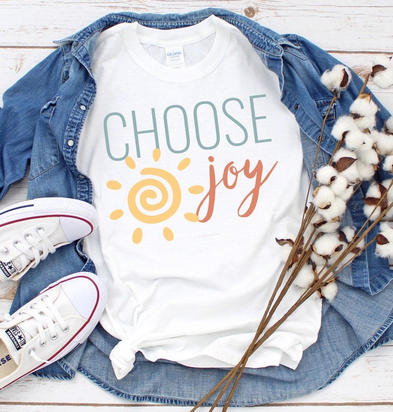 May include: White t-shirt with the text "CHOOSE joy" in blue, orange, and yellow. A stylised sun with a yellow centre and orange rays is to the left of the text.