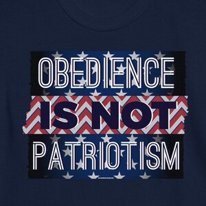 May include: Navy blue t-shirt with the white text "OBEDIENCE IS NOT PATRIOTISM", set against a backdrop of the American flag. The design has a distressed, vintage appearance.