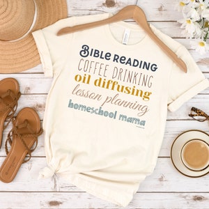 May include: A beige t-shirt with the text "Bible Reading, Coffee Drinking, Oil Diffusing, Lesson Planning, Homeschool Mama" in various colours.
