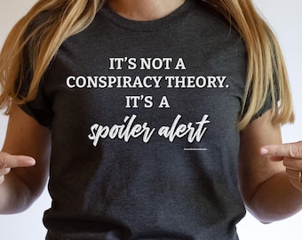 May include: A dark gray t-shirt with white text that reads "It's not a conspiracy theory. It's a spoiler alert."