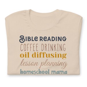 May include: Beige t-shirt with the text "Bible Reading, Coffee Drinking, Oil Diffusing, Lesson Planning, Homeschool Mama" in various colours.