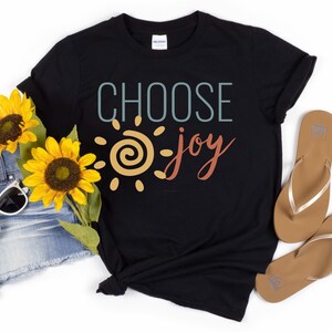 May include: Black t-shirt featuring a graphic design of a sun with a swirl inside and the text "CHOOSE joy" in a colourful retro font.