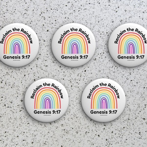 Op de afbeelding: Vier witte ronde knoppen met een regenboog en de tekst "Reclaim the Rainbow" en "Genesis 9:17".