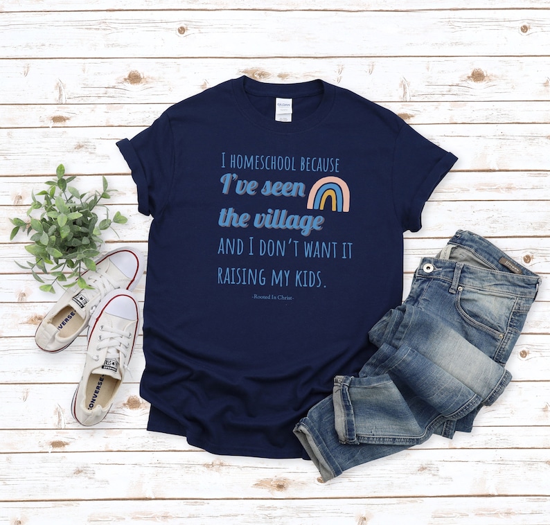 May include: A navy blue t-shirt with the text "I homeschool because I've seen the village and I don't want it raising my kids. Rooted in Christ." and a rainbow graphic.