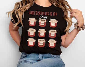 May include: Black t-shirt with the phrase "Homeschooling is my Jam" in red and white. The shirt features illustrations of jam jars with words like "Growing" and "Creating" on them. The shirt is worn by a person.