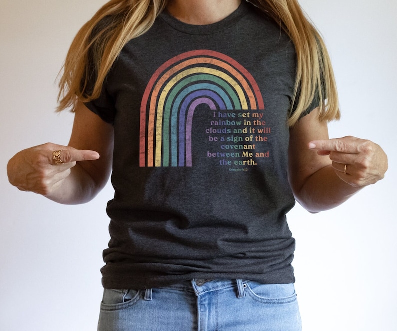 Pu&ograve; includere: Una maglietta grigio scuro con una grafica arcobaleno e il testo "Ho posto il mio arcobaleno nelle nuvole, e sar&agrave; segno dell'alleanza tra me e la terra. Genesi 9:13"