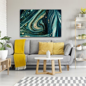 Puede incluir: Pintura abstracta con l&iacute;neas azules y verdes que se arremolinan y purpurina dorada. La pintura est&aacute; colgada en una pared gris sobre un sof&aacute; gris con almohadas amarillas.