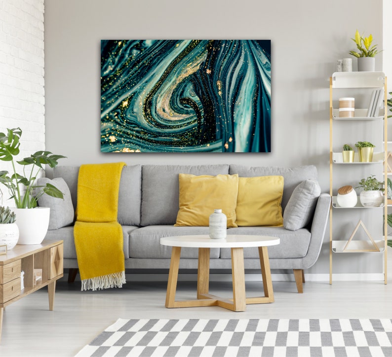 Puede incluir: Pintura abstracta con l&iacute;neas azules y verdes que se arremolinan y purpurina dorada. La pintura est&aacute; colgada en una pared gris sobre un sof&aacute; gris con almohadas amarillas.