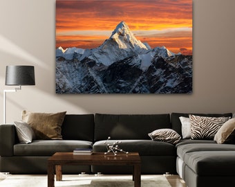 May include: A panoramic view of a snow-capped mountain range with a single peak rising above the others. The sky is a vibrant orange and yellow, creating a dramatic sunset backdrop.