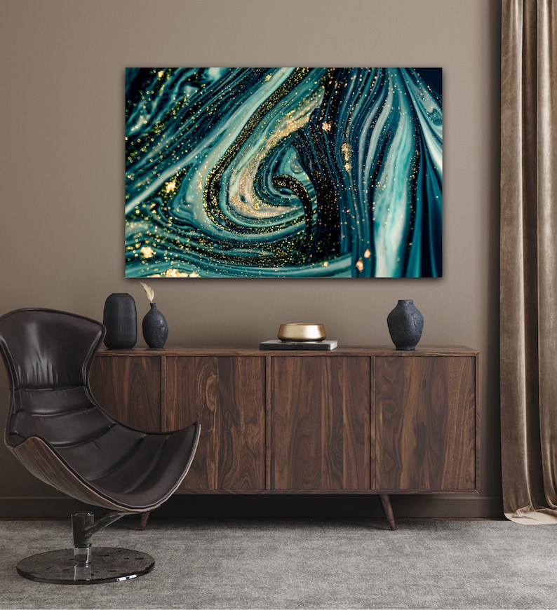 Puede incluir: Impresi&oacute;n de arte abstracto con pintura azul y verde en espiral con detalles de purpurina dorada. La impresi&oacute;n est&aacute; enmarcada y colgada en una pared sobre un armario de madera.