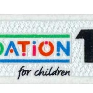 Puede incluir: Un parche blanco con el texto "UEFA FOUNDATION for children" en varios colores. El número "10" en negro está al lado de la palabra "FOUNDATION". La palabra "YEARS" y un grupo de puntos de colores también están presentes.