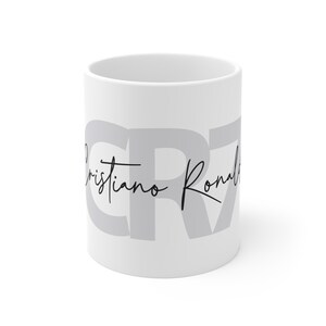 May include: White ceramic mug with the letters "CR7" in gray and the text "Cristiano Ronaldo" in black cursive.