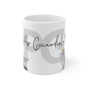 May include: White ceramic mug with the text "Pep Guardiola" and a gray background. The mug features two silver trophies with gold accents.