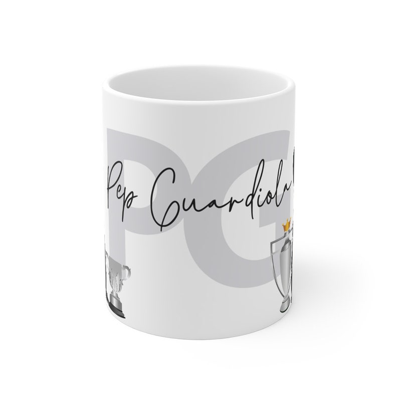 May include: White ceramic mug with the text "Pep Guardiola" and a gray background. The mug features two silver trophies with gold accents.