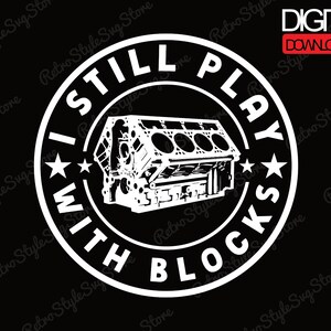 May include: A black and white digital download graphic featuring a stylized engine block. The text "I STILL PLAY WITH BLOCKS" is in a circular design around the engine block, with stars. The words "DIGITAL DOWNLOAD" are in a red rectangle.