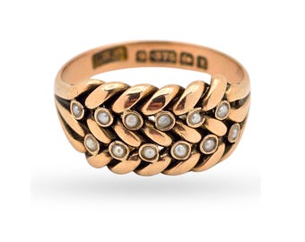 Könnte beinhalten: Ein Ring aus Roségold mit einem geflochtenen Banddesign. Die Oberfläche des Rings ist mit kleinen, runden, weißen Saatperlen verziert, die in die geflochtenen Glieder eingesetzt sind. Die Innenseite des Rings zeigt deutlich eingestanzte Punzierungen.