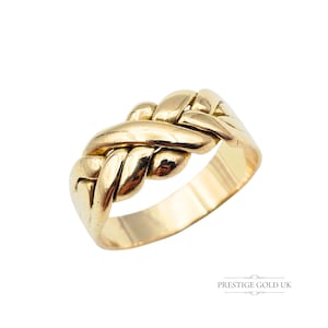 May include: A gold puzzle ring with an interwoven design. The ring has a polished finish and a wide band. The design features multiple interlocking pieces, creating a unique and intricate appearance. The ring is set against a white background.