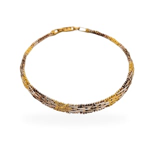 Könnte beinhalten: Ein gold-, silber- und roségoldfarbenes Armband mit einem filigranen, verwobenen Design. Das Armband weist eine Mischung aus Texturen auf, darunter kleine Perlen und flache, gewebte Stränge. Der Verschluss ist goldfarben. Das Schmuckstück ist vor weißem Hintergrund.